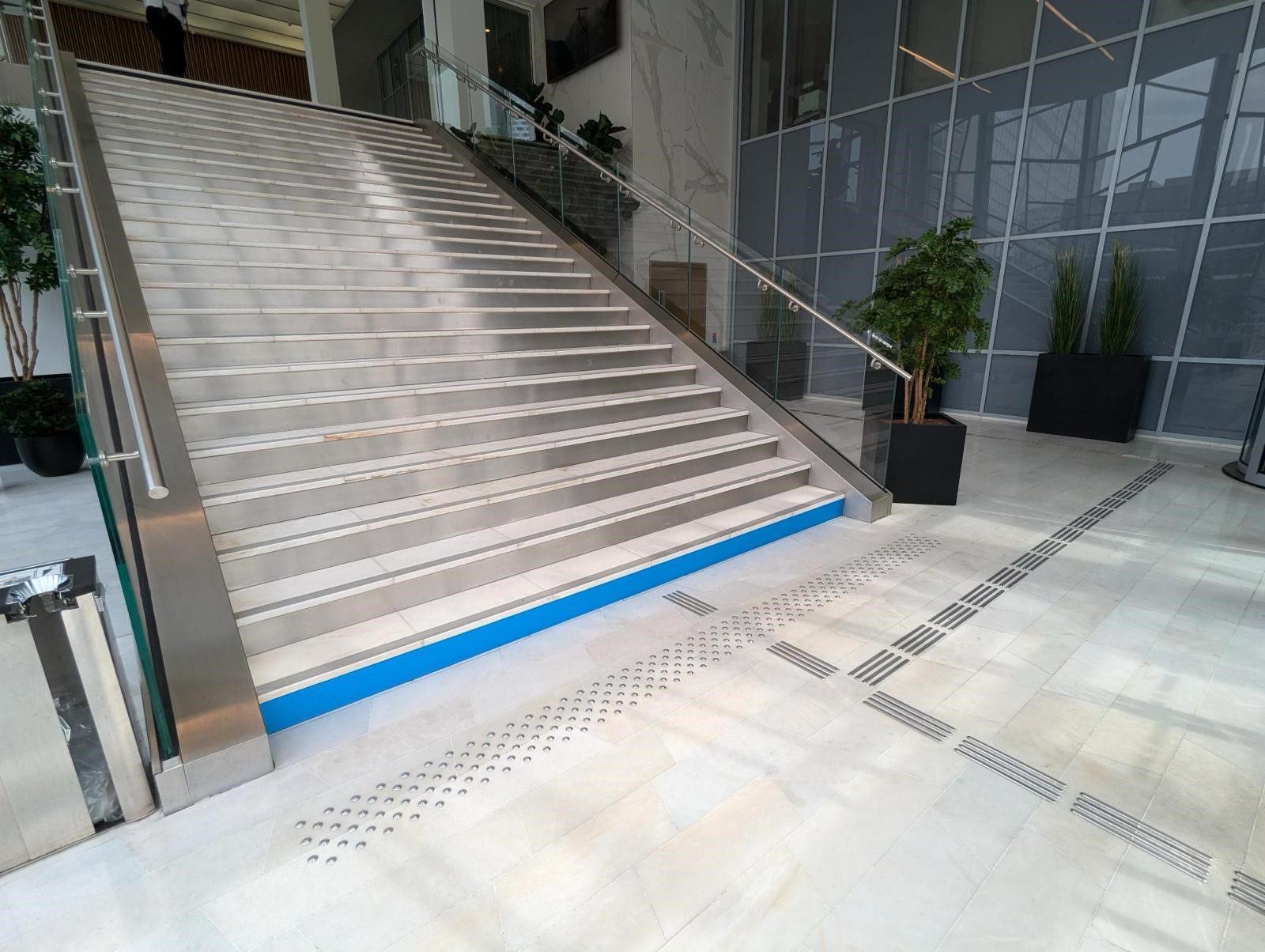 Escalier principal côté Dôme avec une bande d'appel bleue sur la première contremarche et des guides au sol pour se rendre vers l'ascenseur